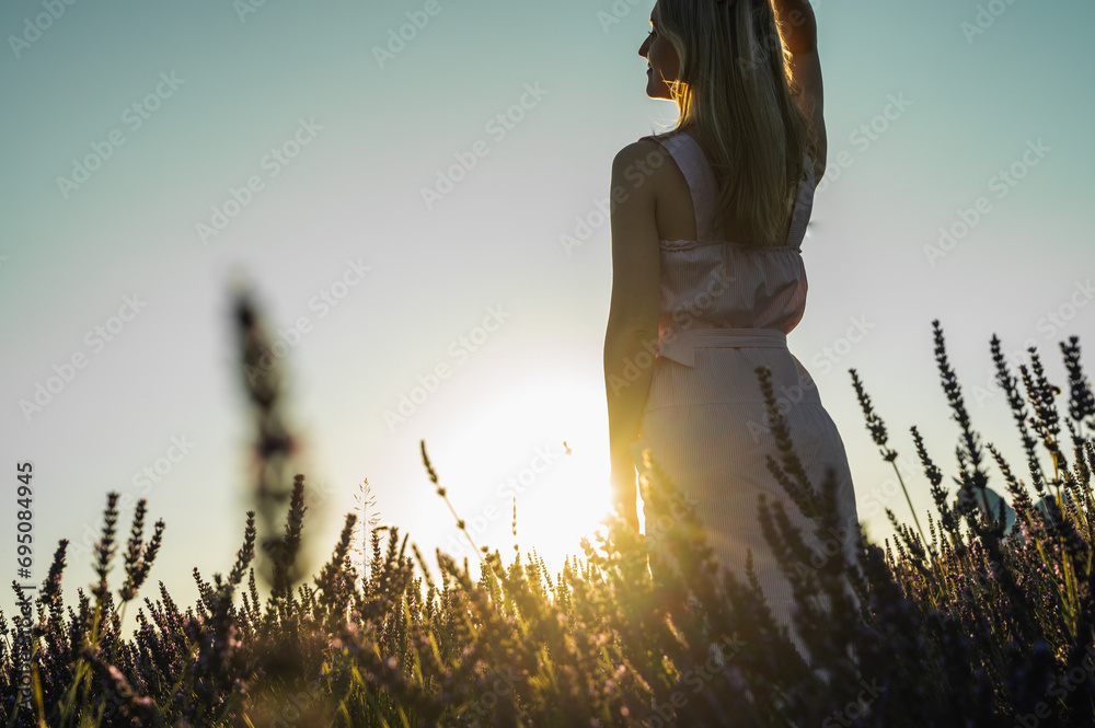 counter portrait of a young girl in a white summer dress on a lavender field, looks from behind, raised her hands to the top of the sun. Blooming lavender in summer. Sunset. Selective focus