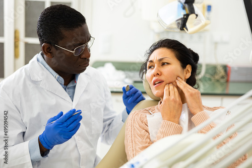 Asian woman patient talking to African American male dentist and complaining about toothache at dental clinic office.. photo