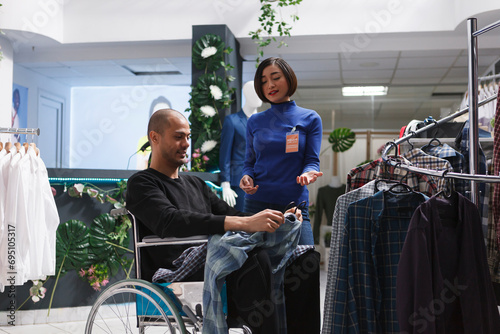 Inclusive clothing store asian woman assistant providing guidance to customer in wheelchair. Arab man in wheelchair buying apparel and getting fashion advice from boutique seller photo