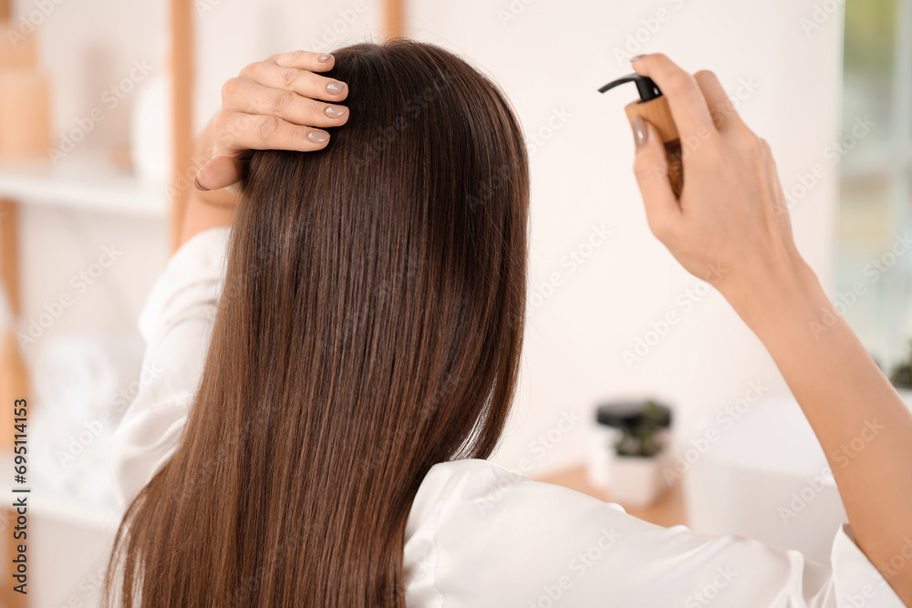 Naklejka premium Young brunette woman applying hair product in bathroom, back view