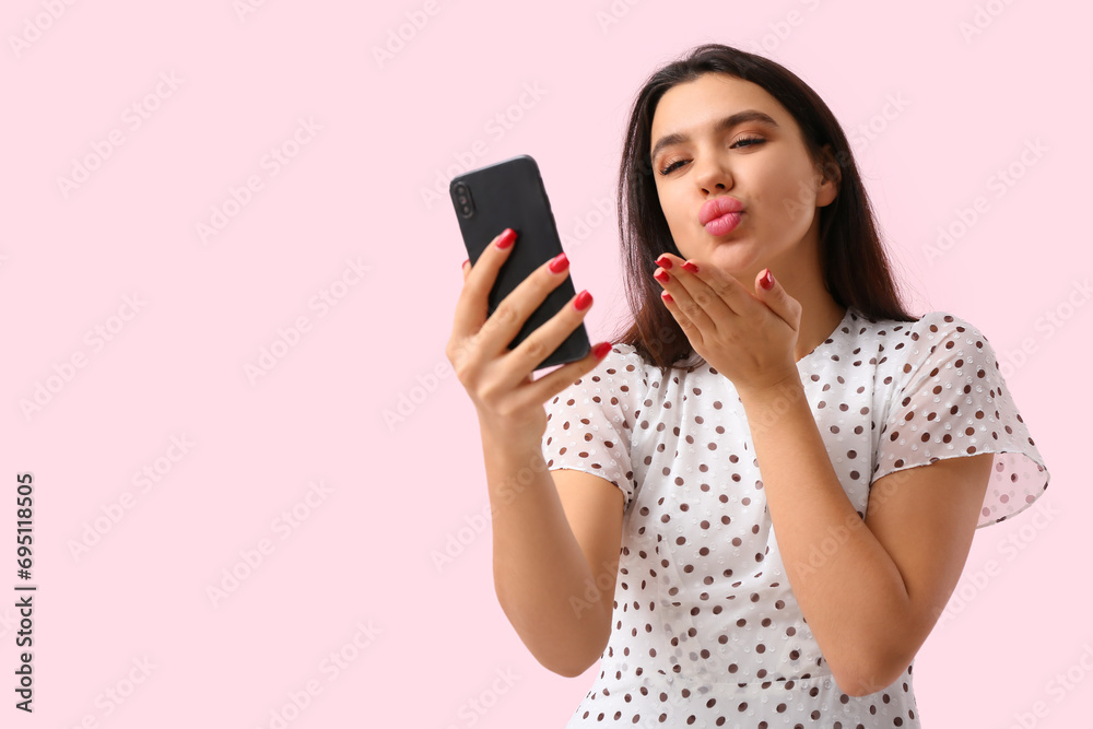 Young woman with mobile phone blowing kiss on pink background. Online dating concept Young woman with mobile phone blowing kiss on pink background. Online dating concept