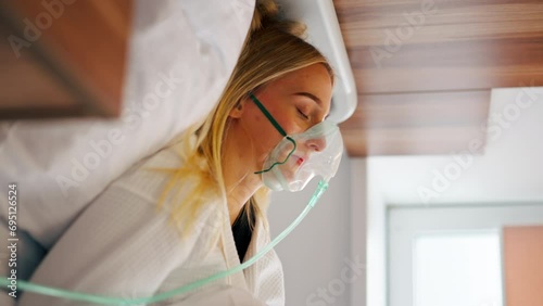 Close-up shot of a girl lying in hospital room wearing an oxygen mask to maintain breathing during illness photo