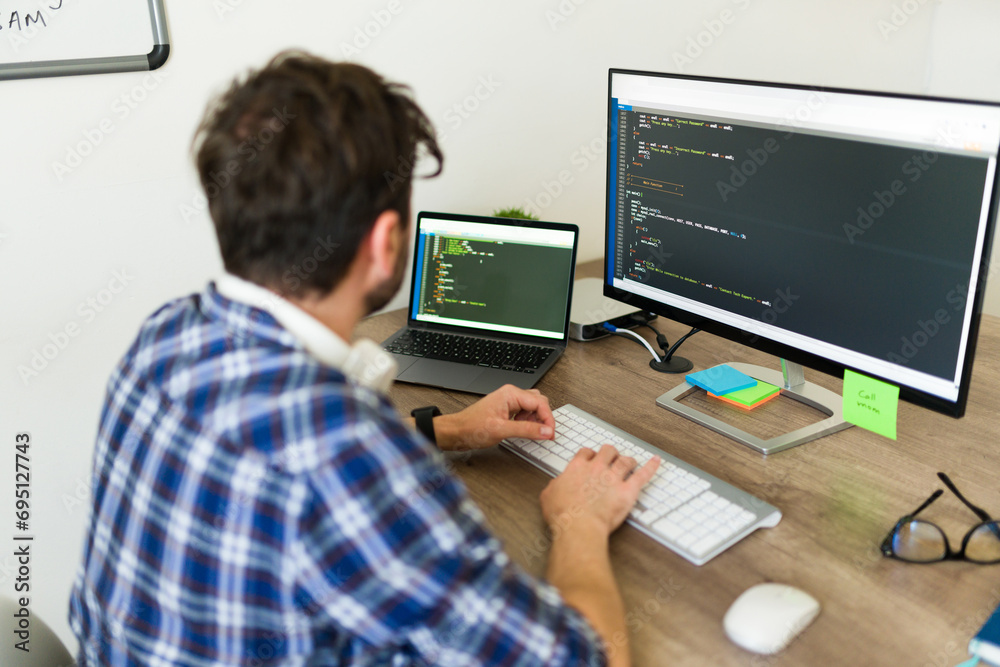 Hispanic programmer typing and writing a new code on the computer while working at the office coding developing new software Hispanic programmer typing and writing a new code on the computer while working at the office coding developing new software