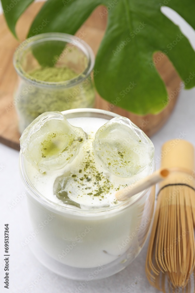 Glass of tasty iced matcha latte, leaf and bamboo whisk on white table Glass of tasty iced matcha latte, leaf and bamboo whisk on white table