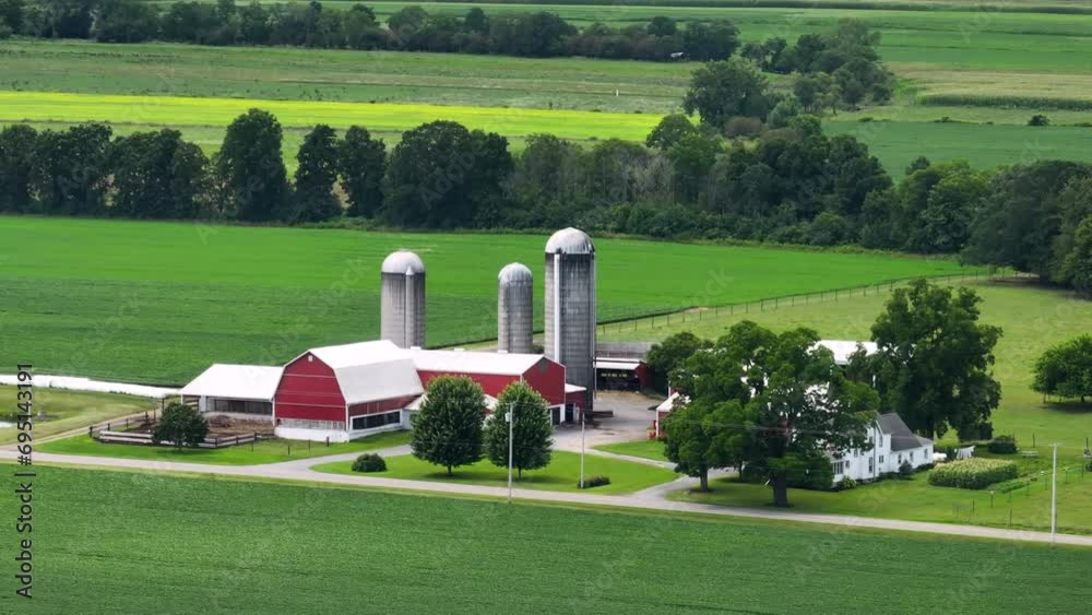 Rural agricultural farm barn and silos between green farmlands in Midwestern USA. American farming landscape