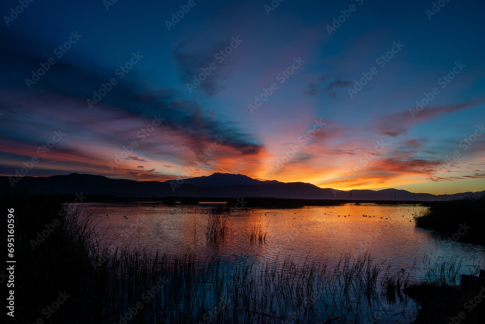 The orange and blue hues of sunrise over a lake with beautiful reflections of a hill and colors