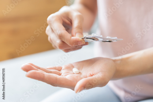 Sick ill asian young woman, girl hand taking tablet pill capsule out from blister pack, painkiller medicine from stomach pain, head ache, pain for treatment, take drug or vitamin at home, health care. photo