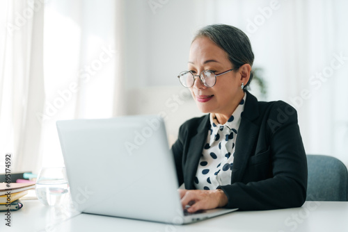 Successful Asian senior businessman sitting working with laptop computer in office.