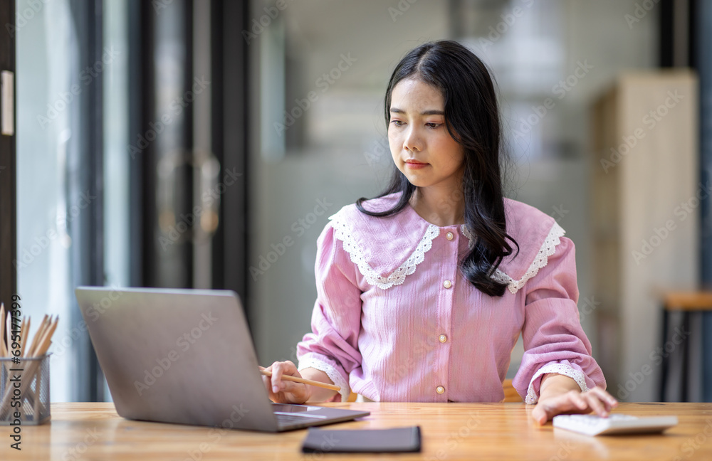 Photo of cheerful joyful young asian business woman in the office working on laptop digital project sitting at desk.