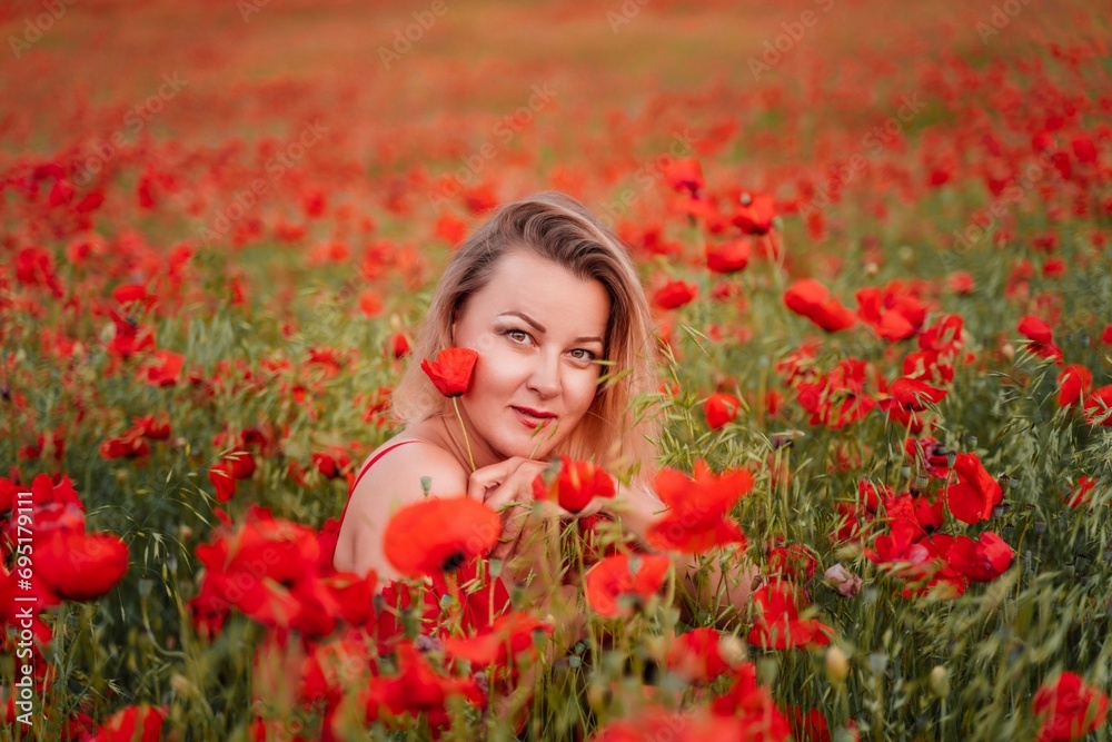 Naklejka premium Happy woman in a red dress in a beautiful large poppy field. Blond sits in a red dress, posing on a large field of red poppies