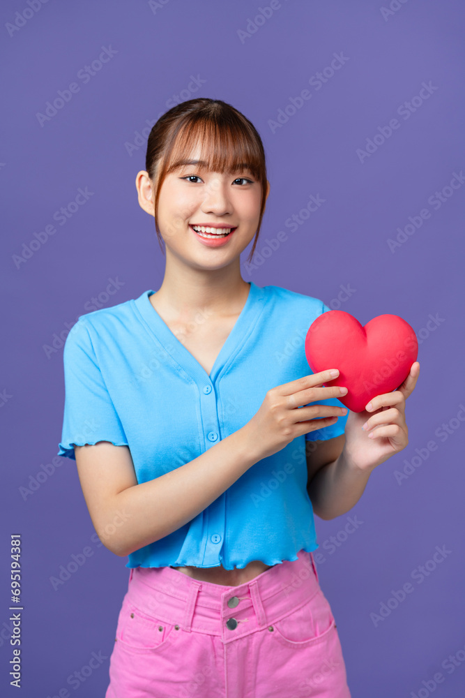 Beautiful woman holds red heart, isolated on purple background Beautiful woman holds red heart, isolated on purple background