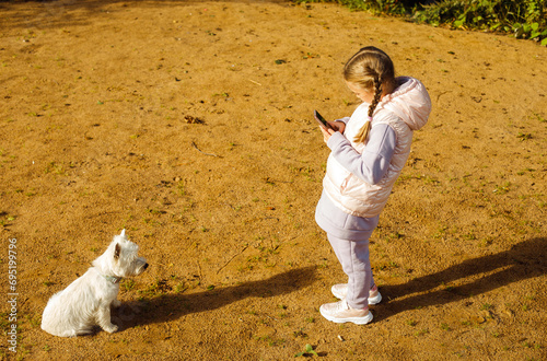 girl plays with a white dog on the beach and takes pictures of her with a smartphone photo