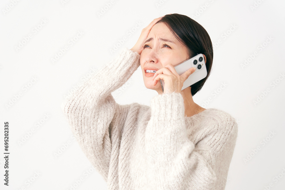 スマホで通話をしながら頭を抱える中年女性 白背景 スマホで通話をしながら頭を抱える中年女性 白背景