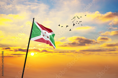 Waving flag of Burundi against the background of a sunset or sunrise. Burundi flag for Independence Day. The symbol of the state on wavy fabric.