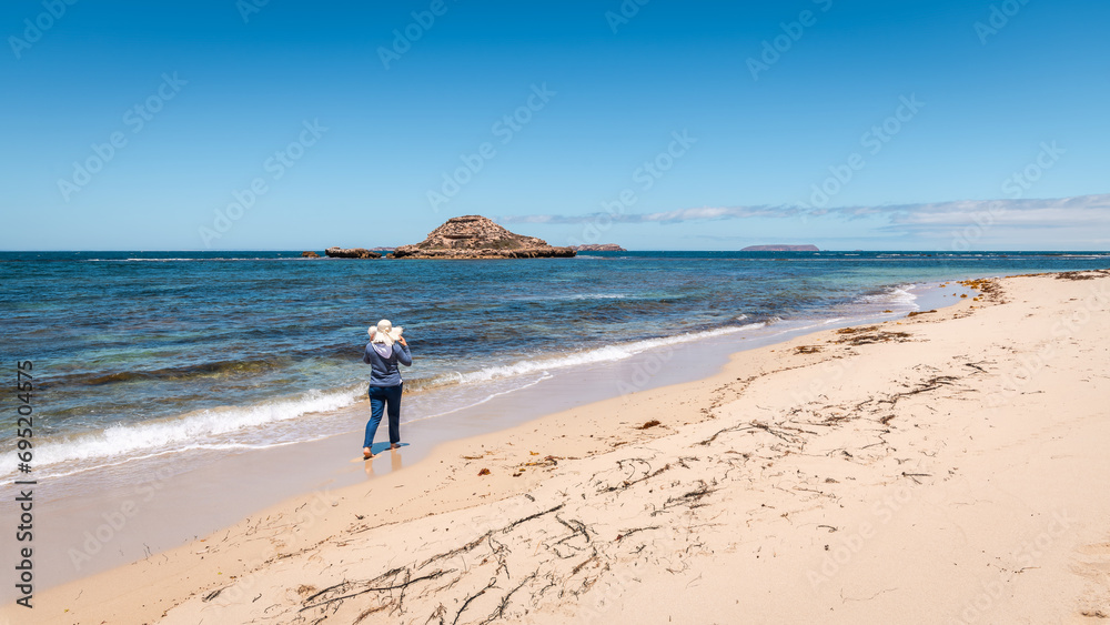 Woman walking along the empty beach while barefeet and wearing a hat, Marion Bay, South Australia