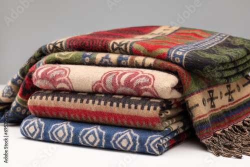 Neatly folded stacks of cashmere stoles, shawls, scarves of different colors. Women's accessory, gift souvenir. On a wooden surface, gray background.