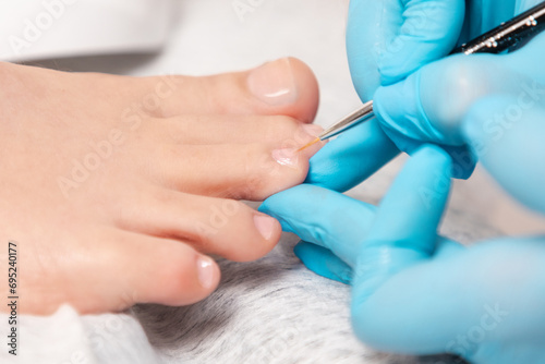 A pedicure master in medical gloves takes care of beautiful female toenails. Close-up. The concept of chiropody and podology