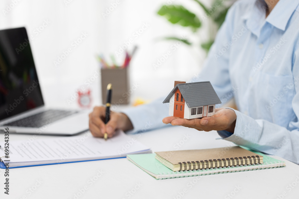 Professional real estate agent signs contract While holding a house. The concept of a home loan contract for housing. Professional real estate agent signs contract While holding a house. The concept of a home loan contract for housing.