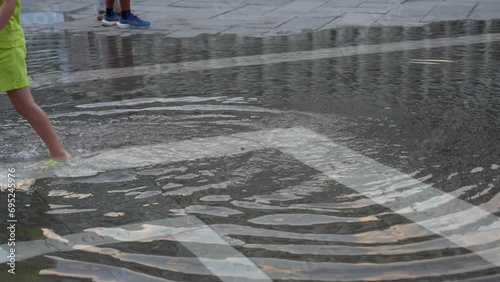 Child in green clothing plays in flooded Piazza San Marco, Venice, Italy photo