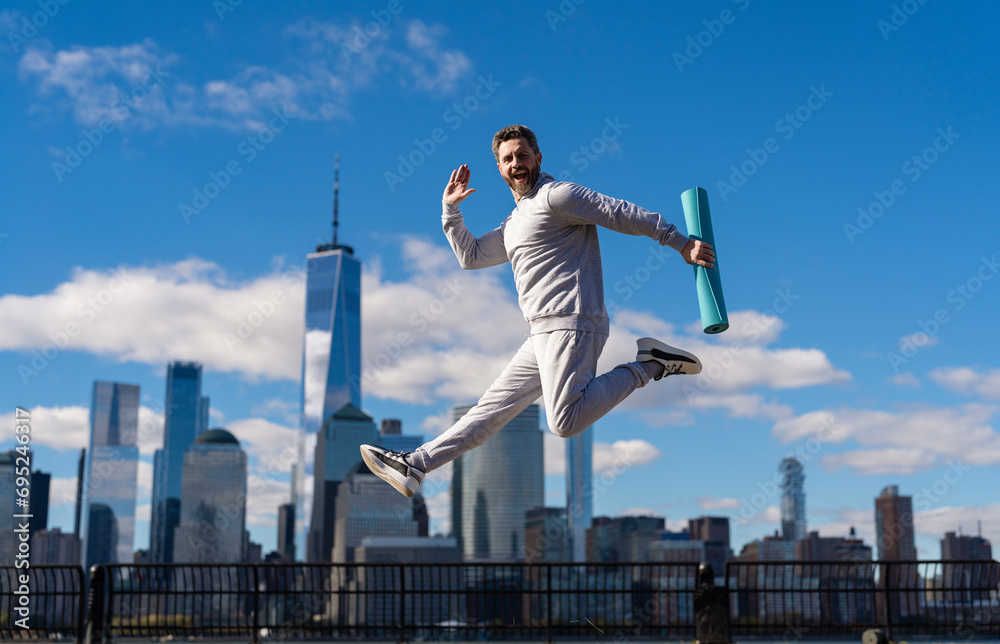 Sport man training outdoor in New York. Healthy lifestyle with daily fitness. Fitness and sport. Man jumping with energy. Sport lifestyle. Sportsman running with fitness mat. Run a race Sport man training outdoor in New York. Healthy lifestyle with daily fitness. Fitness and sport. Man jumping with energy. Sport lifestyle. Sportsman running with fitness mat. Run a race