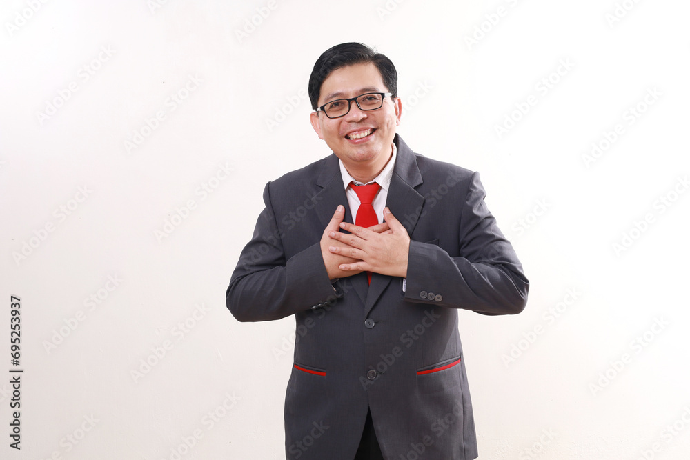 Relieved asian businessman standing while holding chest. Isolated on white background Relieved asian businessman standing while holding chest. Isolated on white background