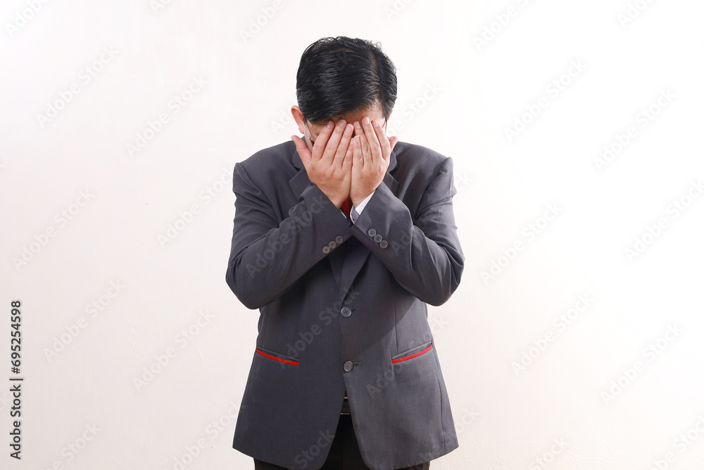 Stressed asian businessman standing while covering face. Isolated on white background