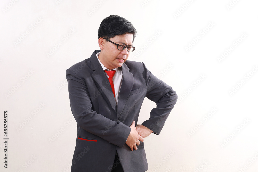Asian businessman grimacing while having pain on his pelvis. Isolated on white
