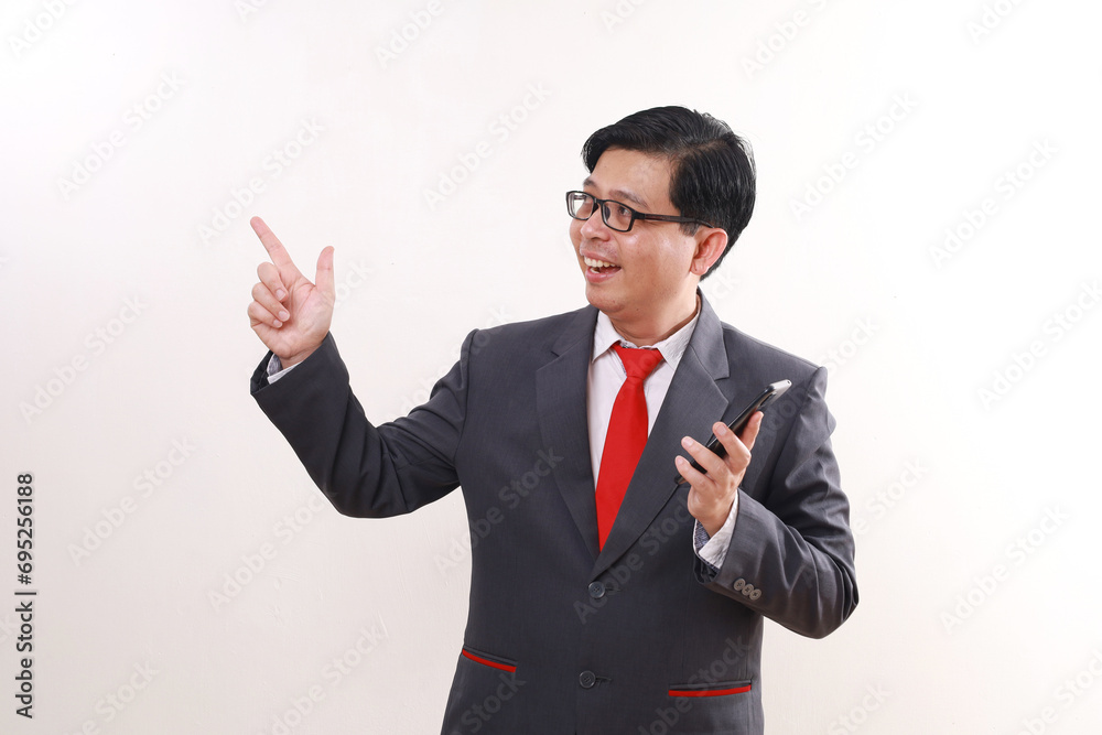 Happy excited asian businessman pointing sideways while holding a cell phone. Isolated on white Happy excited asian businessman pointing sideways while holding a cell phone. Isolated on white