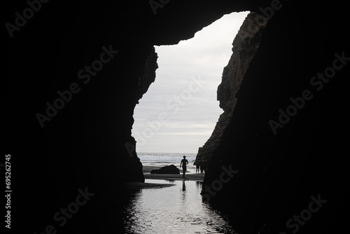 People in a cave on Piha Beach, Auckland, New Zealand