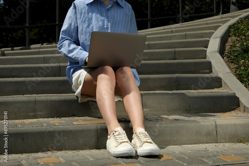 The girl works on a laptop while sitting on the stairs