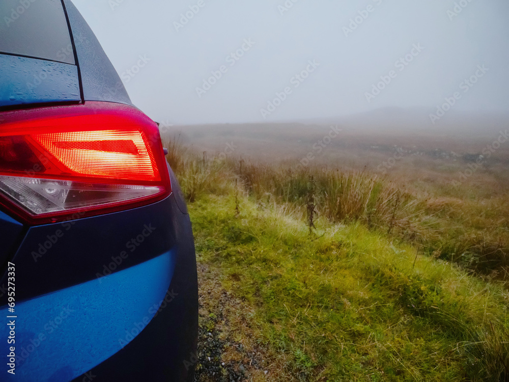 Blue small car parked on a small narrow country road during fog. Dangerous driving conditions due to poor visibility. Nature scene. Selective focus. Travel and tourism.