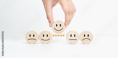 Customer service evaluation and satisfaction survey concepts. The client's hand picked the happy face smile face icon and five star symbol on wooden cube on table.