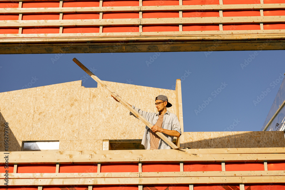 Man as builder or carpenter on construction site of a wooden frame house