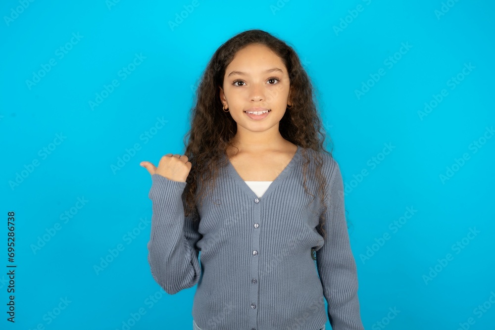 Lovely Beautiful teen girl wearing blue jacket over blue background pointing aside with forefinger, showing at copy space having news about bargains Lovely Beautiful teen girl wearing blue jacket over blue background pointing aside with forefinger, showing at copy space having news about bargains