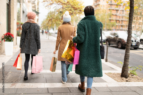 Group of female friends with colorful shopping bags strolling through city streets, enjoying the festive season's sales and winter fashion. photo