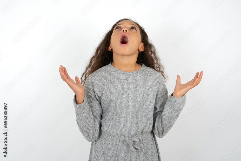 Beautiful teen girl wearing grey dress over white background crazy and mad shouting and yelling with aggressive expression and arms raised. Frustration concept. Beautiful teen girl wearing grey dress over white background crazy and mad shouting and yelling with aggressive expression and arms raised. Frustration concept.