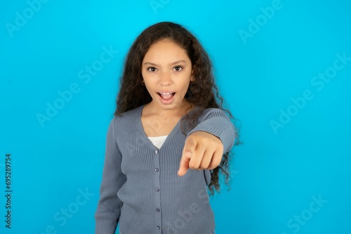 Beautiful teen girl wearing blue jacket over blue background pointing displeased and frustrated to the camera, angry and furious ready to fight with you.