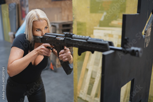 A young beautiful girl with lush breasts is engaged in tactical shooting with an AK47 rifle at a shooting range.