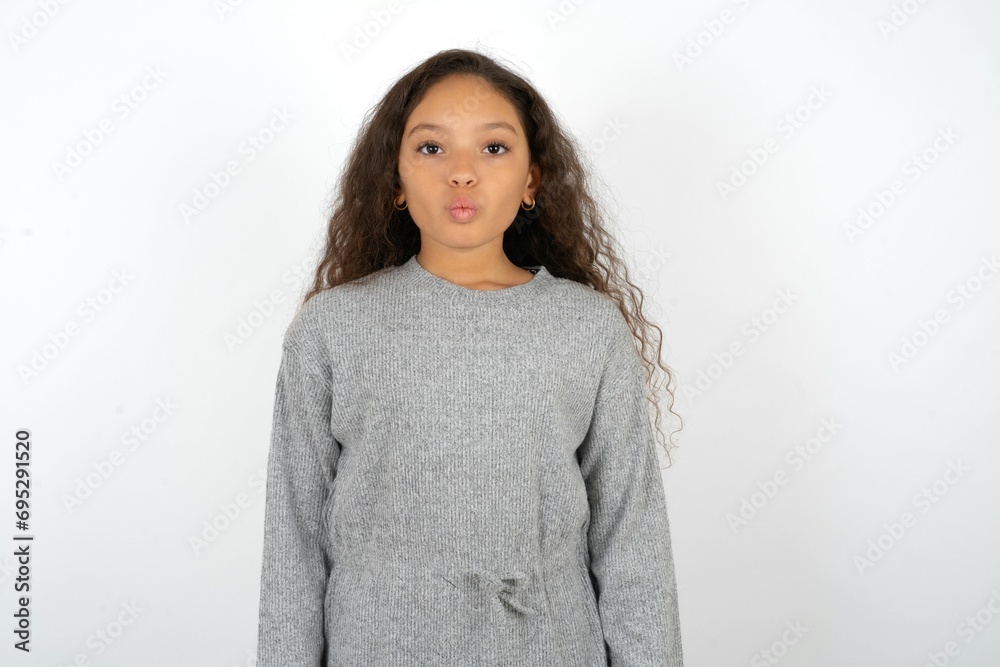 Shot of pleasant looking Beautiful teen girl wearing grey dress over white background, pouts lips, looks at camera, Human facial expressions Shot of pleasant looking Beautiful teen girl wearing grey dress over white background, pouts lips, looks at camera, Human facial expressions