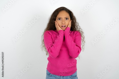 Upset Beautiful teen girl wearing pink sweater over white background touching face with two hands © Roquillo