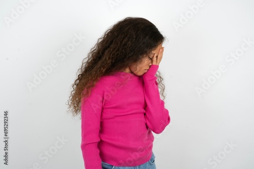 Beautiful teen girl wearing pink sweater over white background with sad expression covering face with hands while crying. Depression concept.