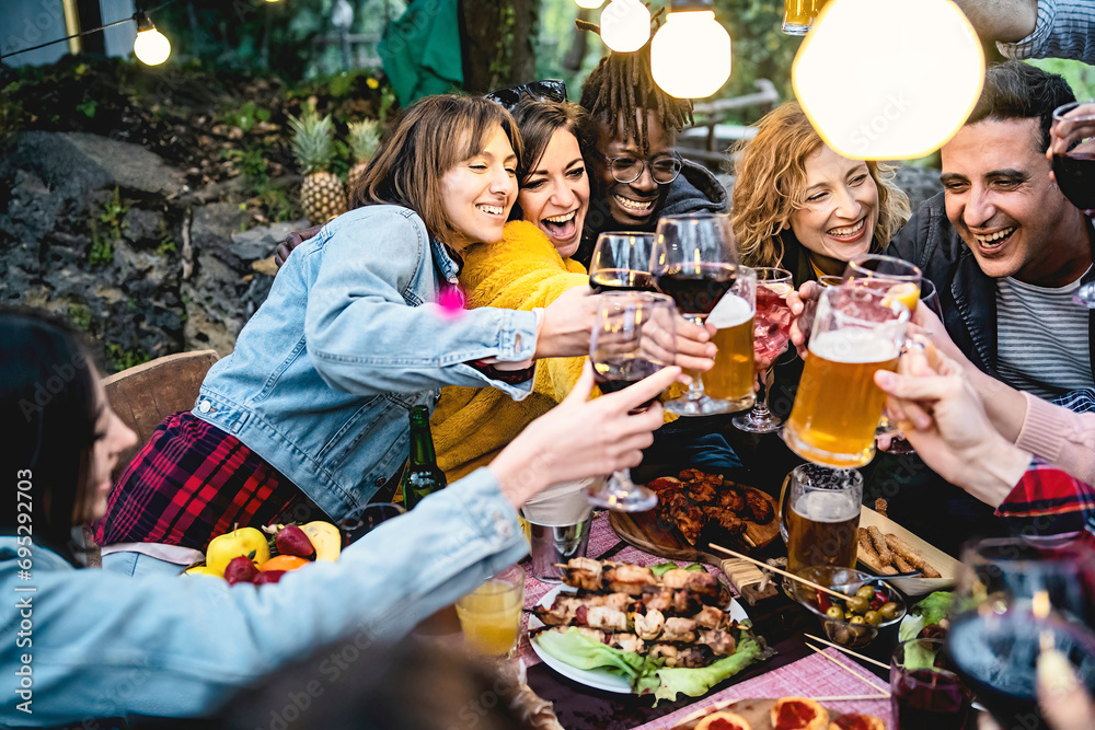 Joyful group of diverse friends toasting with wine and beer, enjoying a barbecue party outdoors, sharing laughter and happiness