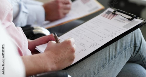 Group of people sitting on chairs and filling out usa visa application form 4k movie slow motion. Assistance in paperwork for travel abroad concept photo