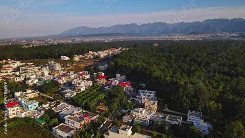 An aerial view of Dehradun, an Indian city during sunrise or sunset, with cloudy weather and rows of residential houses surrounded with greenery. The Himalayan city is surrounded by rainforest.