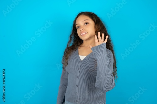 Fotografía Beautiful teen gil wearing casaul clothes over blue background Waiving saying hello happy and smiling, friendly welcome gesture