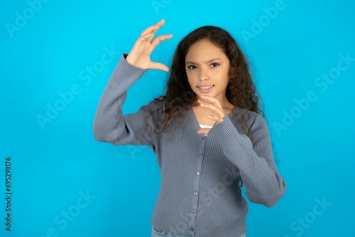 Beautiful teen gil wearing casaul clothes over blue background Shouting frustrated with rage, hands trying to strangle, yelling mad.