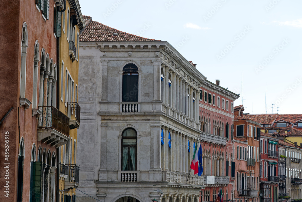 Looking up colorful facades of medieval houses with flags at Italian City of Venice on a cloudy summer day. Photo taken August 6th, 2023, Venice, Italy.