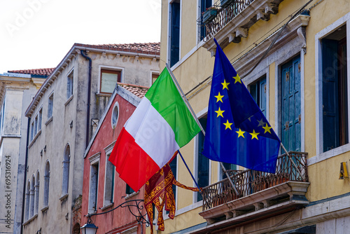 Idyllic view of the old town of Italian City of Venice with waving Italian flag and EU flag on a cloudy summer day. Photo taken August 6th, 2023, Venice, Italy.