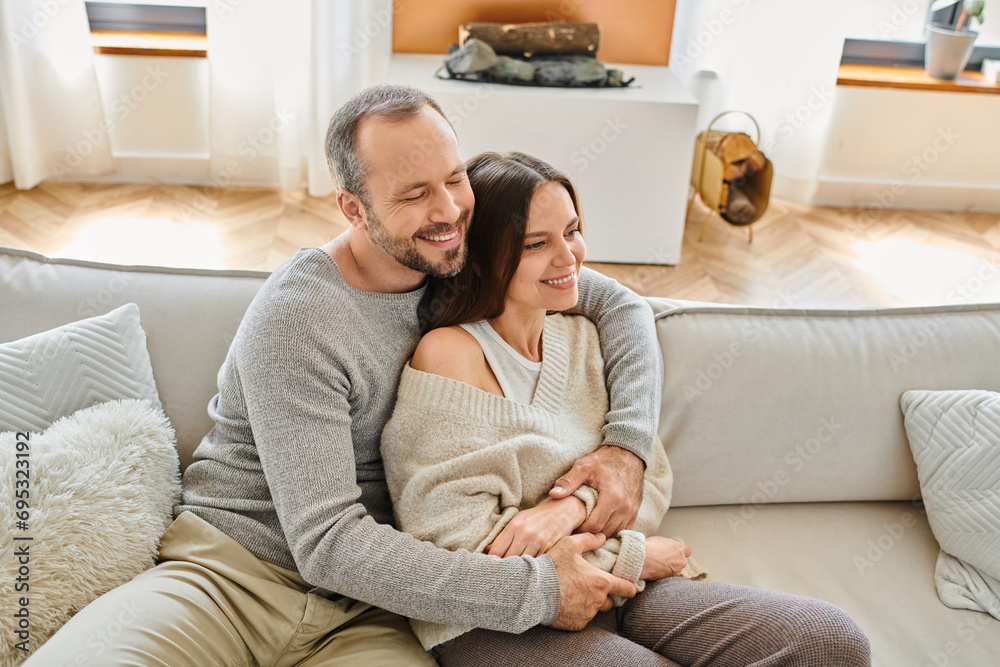 happy man with closed eyes embracing smiling wife of cozy couch in living room, child-free lifestyle happy man with closed eyes embracing smiling wife of cozy couch in living room, child-free lifestyle