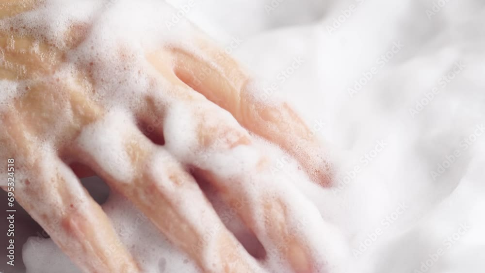 Female hands are washing with soap bubbles. Woman plays with fluffy foam in bathtub, macro. Lady holds handful of soap bubbles, close up.